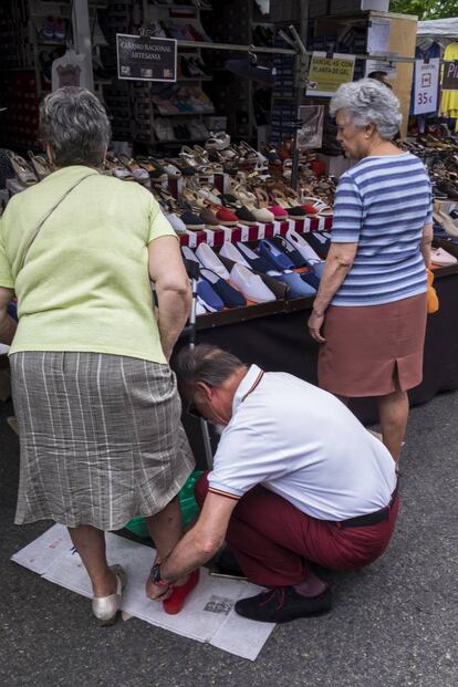 El propietario de un puesto ayuda a una mujer a probarse unos zapatos en el mercadillo de Aluche.