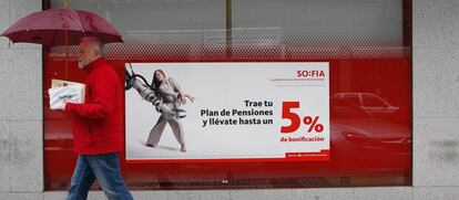 Una persona pasa delante de la una sucursal de Banco Santander donde se promocionan planes de pensiones.