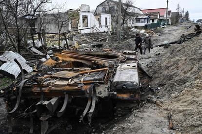 Dos civiles caminan entre los restos de un tanque ruso carbonizado y viviendas destruidas en el pueblo de Zalissya, al noreste de Kiev, el martes. La responsable del comité de derechos humanos del Parlamento ucranio, Mikita Poturayev, ha acusado este miércoles a Moscú de haber deportado a medio millón de personas de Ucrania a Rusia.