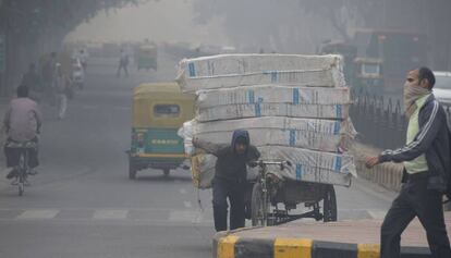 Un hombre con el rostro cubierto camina por una calle de Nueva Delhi cibierta por una nube de contaminación.