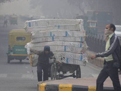 Un hombre con el rostro cubierto camina por una calle de Nueva Delhi cibierta por una nube de contaminación.