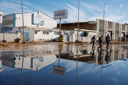 Tres hombres caminan por una calle anegada en el polígono de Catarroja, Valencia.