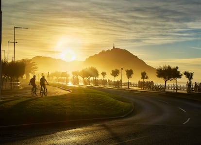 Dos ciclistas pedalean en San Sebastián mientras el sol se pone detrás del Monte Urgull.
