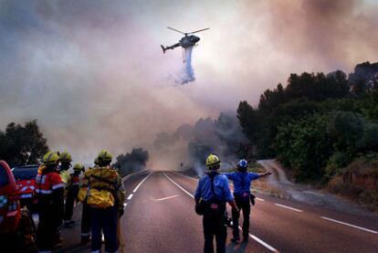 Varios bomberos observan cómo un helicóptero descarga agua sobre el terreno incendiado, ayer en La Riba (Tarragona).