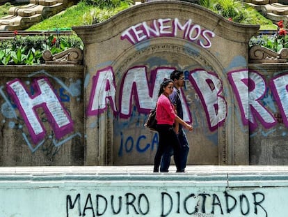 Una pareja pasea frente a un grafiti de protesta contra el Gobierno venezolano.