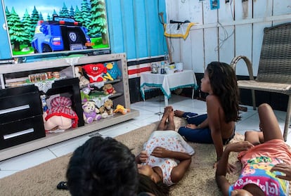 Em foto de 24 de março de 2017, Alice (sentada) assiste a desenhos na TV, hoje principal lazer das crianças indígenas, proibidas de se aproximar do rio.