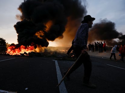 A man walks near a fire, as farmers block the AP-7 highway during a protest over price pressures, taxes and green regulation, near Girona, Spain, February 6, 2024.