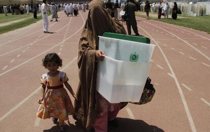 Una empleada de la organizaci&oacute;n de las elecciones transporta, acompa&ntilde;ada de su hija, una de las urnas en Peshawar.