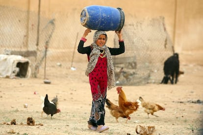 A displaced Syrian child, who fled the countryside surrounding the Islamic State (IS) group stronghold of Raqa, carries a barrel over her head as she walks at a temporary camp in the village of Ain Issa on April 28, 2017. / AFP PHOTO / DELIL SOULEIMAN