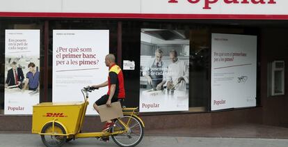 Un repartidor pasa ante una oficina del Banco Popular en el Paseo de Gracia esquina con la calle Aragón de Barcelona.