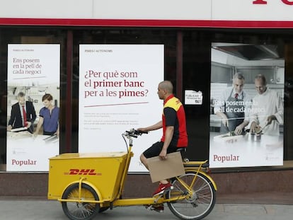 Un repartidor pasa ante una oficina del Banco Popular en el Paseo de Gracia esquina con la calle Aragón de Barcelona.