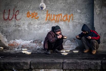 Dos migrantes se alimentan con comida recibida por voluntarios, en un almacén a las afueras de Belgrado (Serbia).