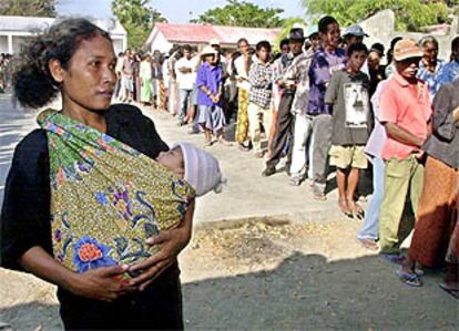 Una timorense sujeta a su bebé mientras mira la cola que tendrá que aguardar para votar.