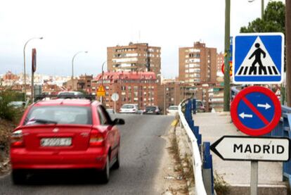 La fotografía está tomada en el puente de Praga. En ella se aprecian tres señales en un poste. La primera de un paso de peatones que no existe. La segunda, una advertencia que prohíbe estacionar en la calzada. Como se aprecia, el carril no es lo suficientemente ancho como para que un vehículo aparque en él. El tercero indica un acceso a la ciudad, cuando ya estamos en el centro de Madrid.