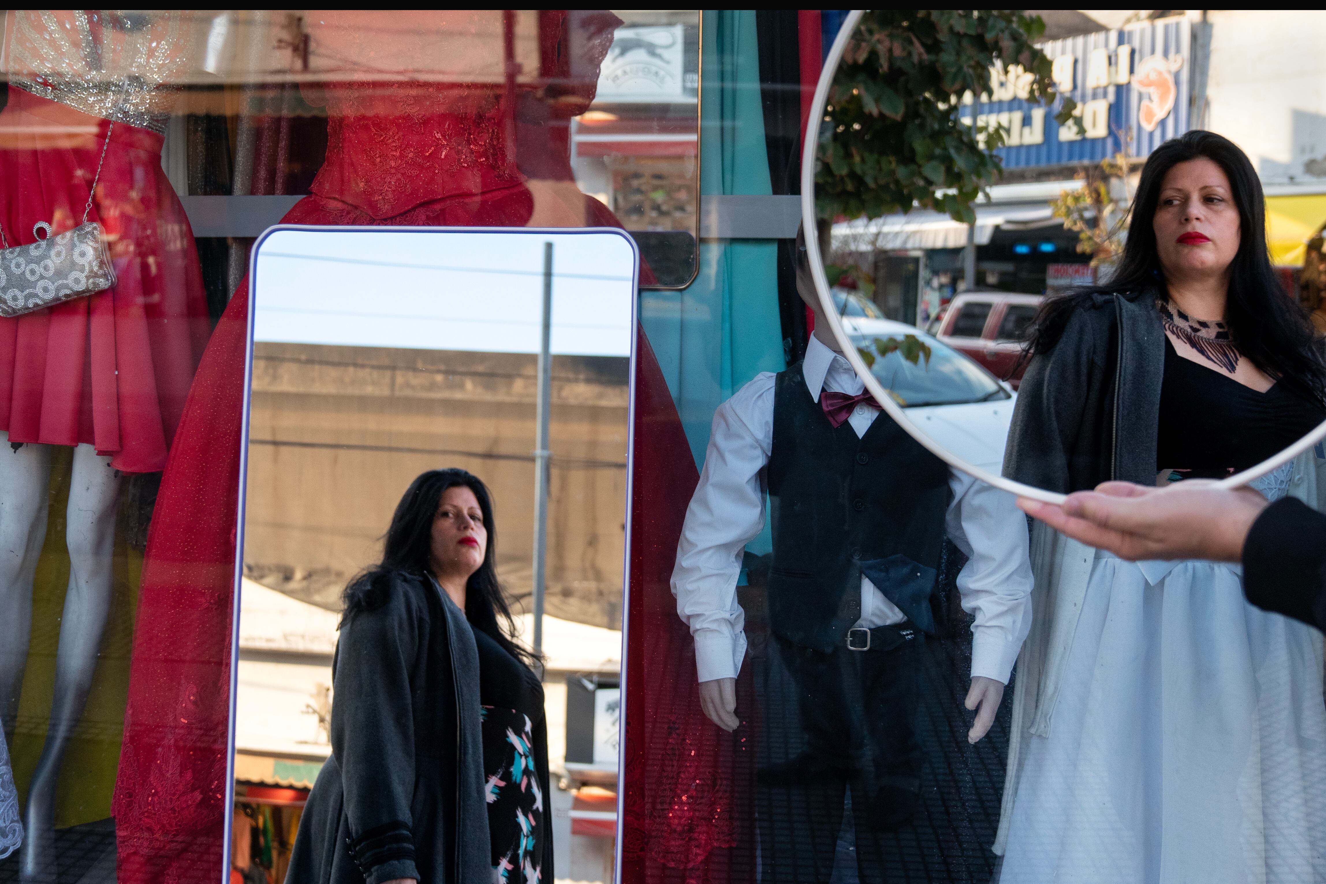 Dolores Reyes se refleja en los espejos que ofrece un vendedor callejero frente a una tienda de ropa para fiestas en la zona comercial de Liniers, en Buenos Aires.