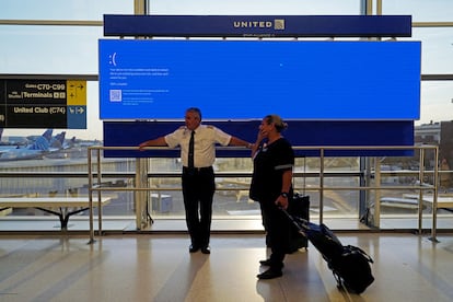 Los empleados de United Airlines esperan junto a un monitor de salidas que muestra una pantalla de error azul, en el Aeropuerto Internacional de Newark.