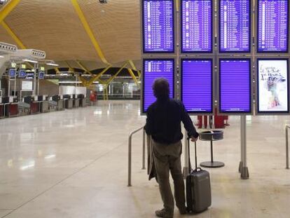 Un pasajero, con su maleta, consulta unos paneles informativos con los horarios de las salidas de los vuelos. 