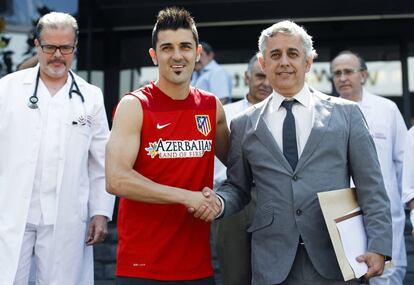 El delantero David Villa y el m&eacute;dico del Atl&eacute;tico de Madrid, Jos&eacute; Mar&iacute;a Villal&oacute;n (d), a la entrada de la cl&iacute;nica donde el jugador pas&oacute; reconocimiento m&eacute;dico. El Barcelona y el Atl&eacute;tico llegaron a un acuerdo para el traspaso del delantero internacional al club madrile&ntilde;o.