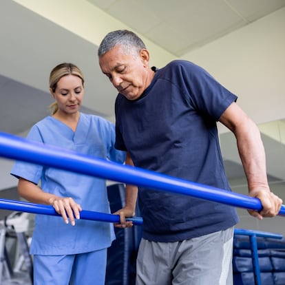 Latin American man doing physical therapy and walking on bars with the assistance of his physical therapist