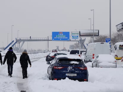 Varias personas pasean cerca de los vehículos atascados en la Carretera de Colmenar, M-607, el sábado en Madrid.