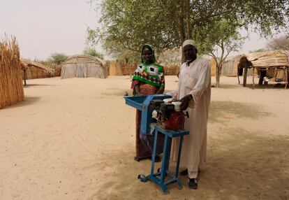 El líder de la comunidad y una hija de Hadje Gombo posan con el molinillo que las mujeres utilizan para machacar los tomates u okras secos y así poder conservarlos en buen estado más tiempo.