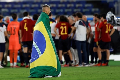 Richarlison, enfundado en una bandera de Brasil mientras los jugadores españoles hacen un corro.