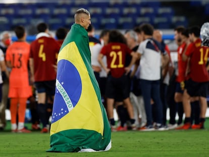 Richarlison, enfundado en una bandera de Brasil mientras los jugadores españoles hacen un corro.