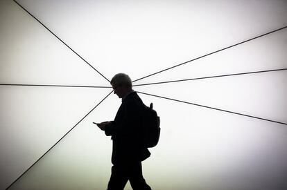 Un hombre pasa junto a una pantalla mientras utiliza su teléfono móvil en el Mobile World Congress 2019.