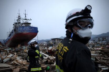 Dos bomberos caminan entre escombros ante un buque arrastrado por el tsunami tierra adentro en Kesennuma.