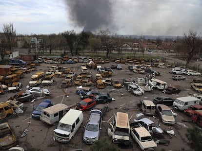 Vehículos destrozados cerca de la planta metalúrgica de Azovstal, desde la que emerge al fondo una columna de humo.