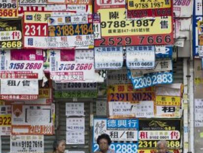 Tres mujeres sientan delante de una tienda cubierta por anuncios de venta y alquiler en Hong Kong.