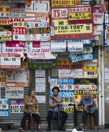 Tres mujeres sientan delante de una tienda cubierta por anuncios de venta y alquiler en Hong Kong.