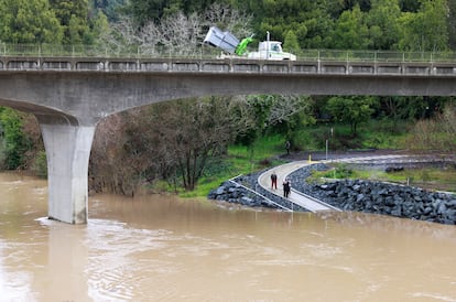 El fenómeno meteorológico ha dejado sin electricidad a miles de hogares. Ante la amenaza de inundaciones repentinas y deslizamientos de tierra, las autoridades han solicitado a la población resguardarse. En la imagen, habitantes de Guerneville caminan cerca del río Russian, que se encuentra desbordado.