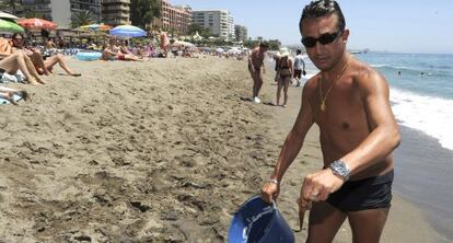 Un ba&ntilde;ista muestra una medusa capturada en la playa de La Venus, en Marbella.