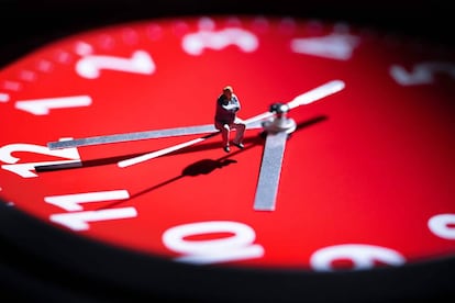 Figurita sentada en la saeta de un reloj.