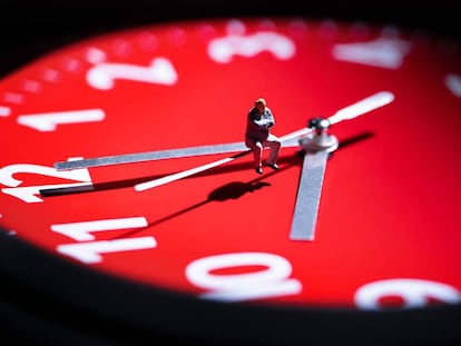 Figurita sentada en la saeta de un reloj.