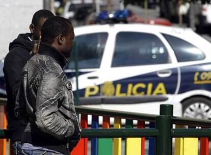 Dos inmigrantes pasan junto a un coche patrulla del Cuerpo Nacional de Policía que vigilaba ayer el barrio de Lavapiés.