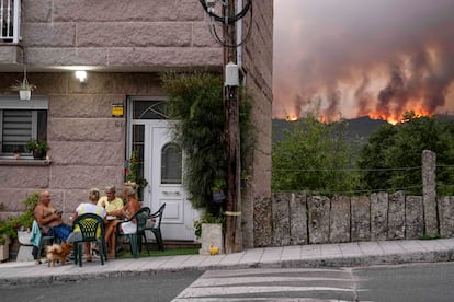 Vecinos de Carballeda de Avia (Oursense) juegan a las cartas el sábado mientras avanza un incendio forestal.