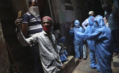 Un hombre con mascarilla se hace un 'selfie' mientras que trabajadores de salud recopilan muestras de residentes de Dharavi, uno de los barrios marginales más grandes de Asia, durante el confinamiento para evitar la propagación del coronavirus en Bombay (India).