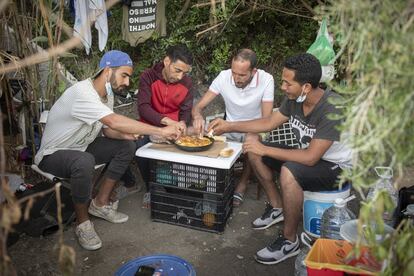 Cuatro amigos que viven en el bosque comen un tayín de verduras que han cocinado en la playa para evitar riesgos de incendio. Muchas personas prefieren permanecer en la calle ante el temor de ser devueltos a Marruecos si acuden a las instalaciones que gestiona el Ejecutivo local en el polígono industrial de El Tarajal, junto a la frontera.