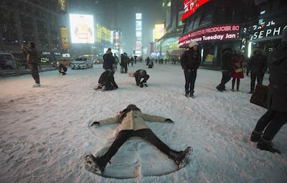 Uma mulher desenha o formato de anjo, deitada sobre a neve no meio da Times Square, em Nova York.