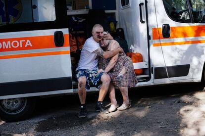 Dos heridos se agarran sentados en una ambulancia después de los bombarderos.