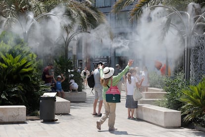 Varios turistas tratan de mitigar el calor bajo una nube de agua vaporizada en la plaza de la Reina de Valencia, este domingo.