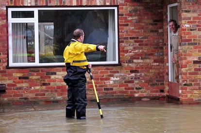 Un bombero habla con un vecino que se asoma a la puerta de su casa en  Wraysbury afectado por las inundaciones. 