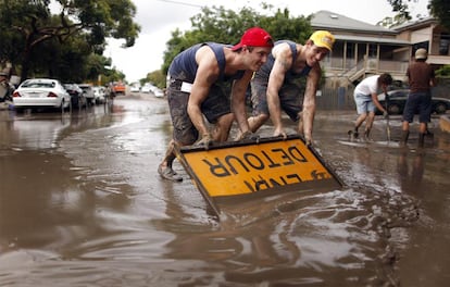 Un par de jóvenes utilizan una señal para limpiar el barro después de que el agua de las inundaciones haya desparacido ya del barrio Westend de Brisbane. Otros suburbios continúan sin embargo empantanados, mientras pequeños pueblos esperan más lluvias y las previsiones metereológicas anuncian posibles ciclones.