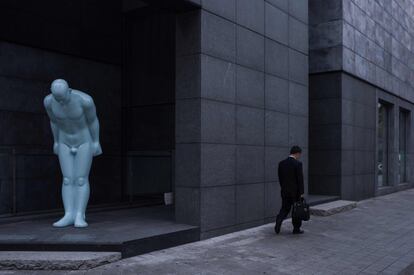Un hombre camina por delante de una estatua en posición de reverencia, en Seul (Corea del Sur).