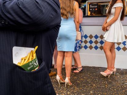 Un hombre esconde un cucurucho de patatas en su elegante chaqueta de raya diplomática en las carreras de Epsom.