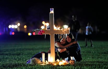 People comfort each other as they sit and mourn at one of seventeen crosses, Feb. 15, 2018