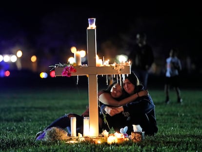 People comfort each other as they sit and mourn at one of seventeen crosses, Feb. 15, 2018, after a candlelight vigil for the victims of the shooting at Marjory Stoneman Douglas High School, in Parkland, Fla.
