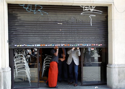 Unos trabajadores bajan la persiana de un bar en Barcelona.